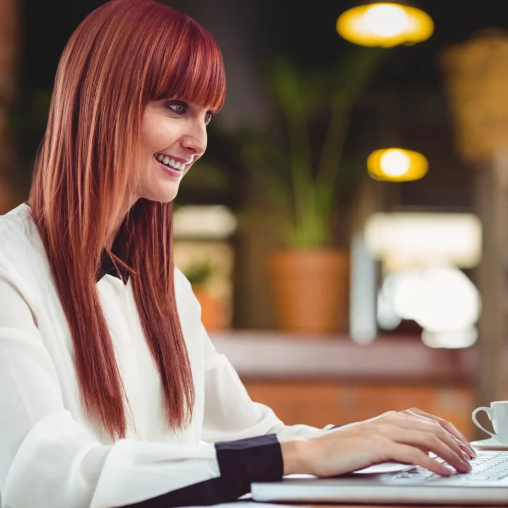 Femme souriante tapant sur un ordinateur portable.